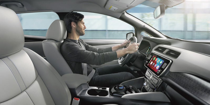 Interior view of a person driving a modern car with touchscreen display.