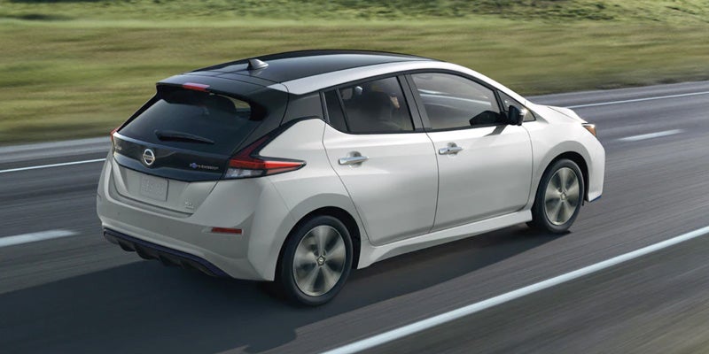 Rear-side view of a white Nissan Leaf car driving on a highway.
